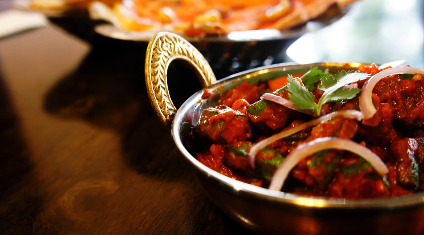 A brass kadai of Malabar Palace curry, garnished with onion and coriander
